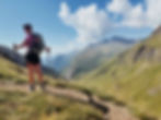 Hiker with backpack, hat, and hiking poles standing on a mountain and gazing into the distance—perfect gear for a day trip, inspired by the ultimate packing list for hiking in the mountains.