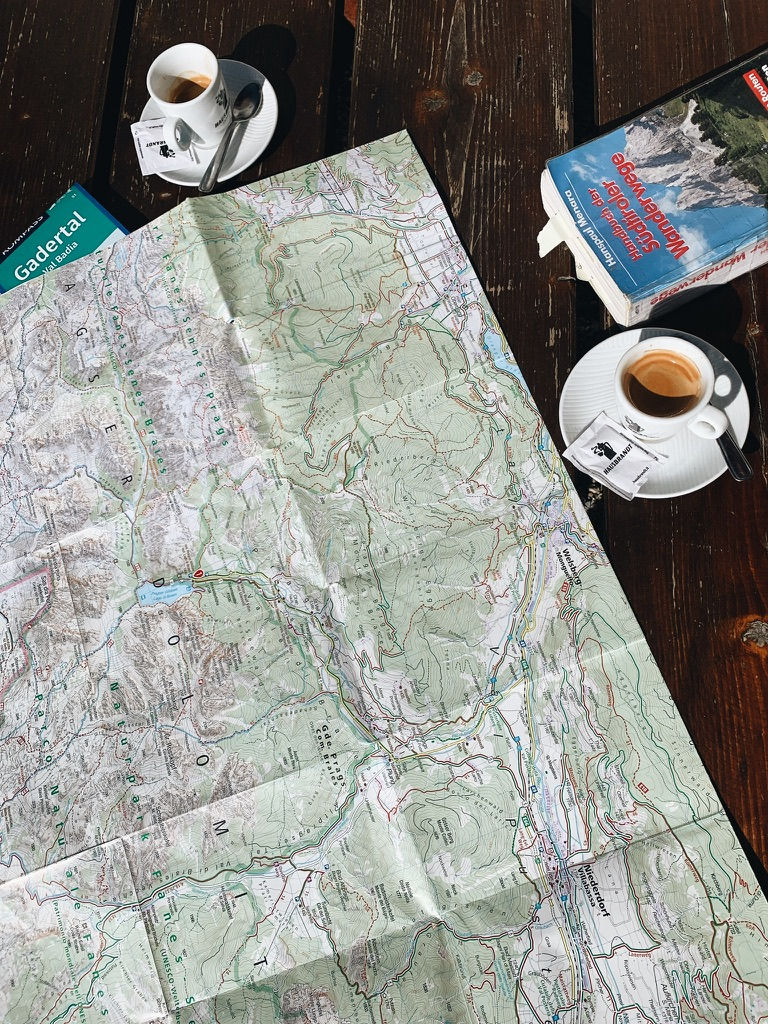 Ausgebreitete Wanderkarte neben zwei Cafés – wichtige Vorbereitung für Tageswanderung in den Bergen, Planung der Route und Einkehrmöglichkeiten