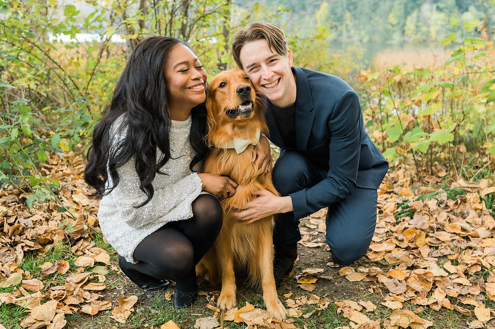 Couple crouching in autumn leaves, smiling with a golden retriever wearing a bow tie, capturing a joyful moment.