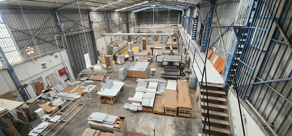Geniş bir atölyede iki işçi, Akrilik Corian ahşap ve panel parçaları arasında çalışıyor; duvarlarda mavi merdivenler, kutularda Hanex yazısı.