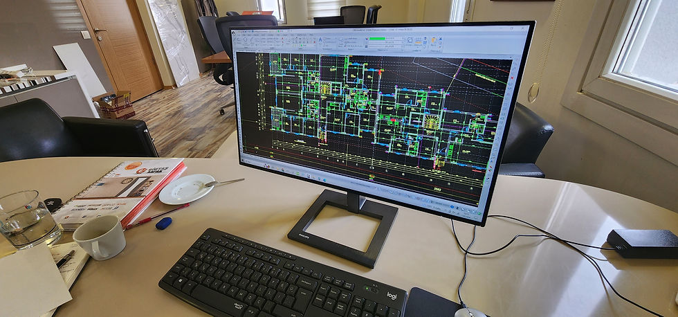 Ofiste masada, Philips monitörde renkli bir CAD kat planı açık; klavye, notlar ve bardaklar yan yana.
