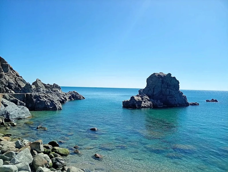 Spiaggia con sabbia chiara, mare turchese, ombrellone rosso e sdraio.
