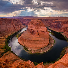 Long-exposure landscape photography of Horseshoe Bend in Page, Arizona. Rainy weather enhances the deep colors of the canyon walls and the emerald curve of the Colorado River.
