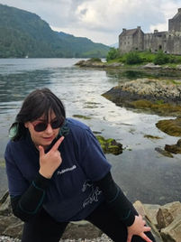 Female tour guide striking a pose with sunglasses on with an epic Scottish castle in the background.