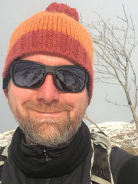 Tour guide wearing a woollen hat and sunglasses in a snowy Scottish landscape