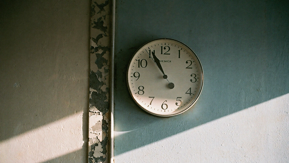 Reloj de pared antiguo en un muro descascarado, iluminado de lado