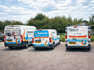 Three Endeavour Plumbing & Heating vans parked on gravel under a cloudy sky, with trees behind.