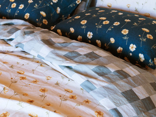 Floral and gingham linen bedding layered on a bed with patterned linen pillowcases and sheets.