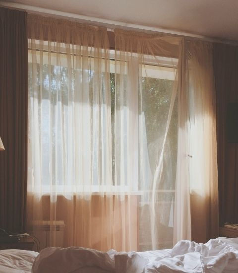 Soft linen bedding beside sheer curtains in warm morning light