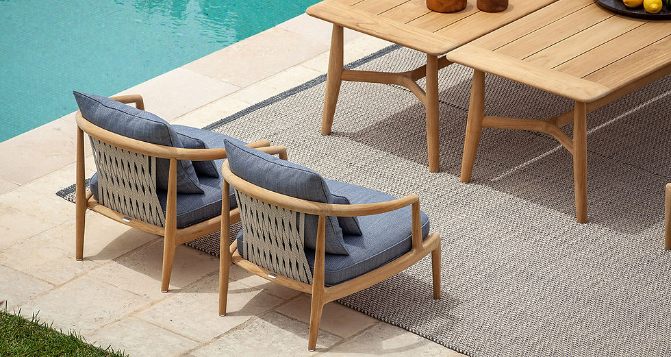 Two wooden chairs with a woven back next to a swimming pool Two wooden tables sit nearby on a woven rug.
