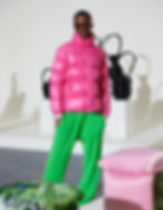 A modern wears sunglasses, a bright pink puffer jacket and green sweat pants. 