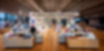 An image of a boutique shop. There are wooden floors and a concrete ceiling, as well as a series of pedestals that hold books, notebooks, bags, and other items.