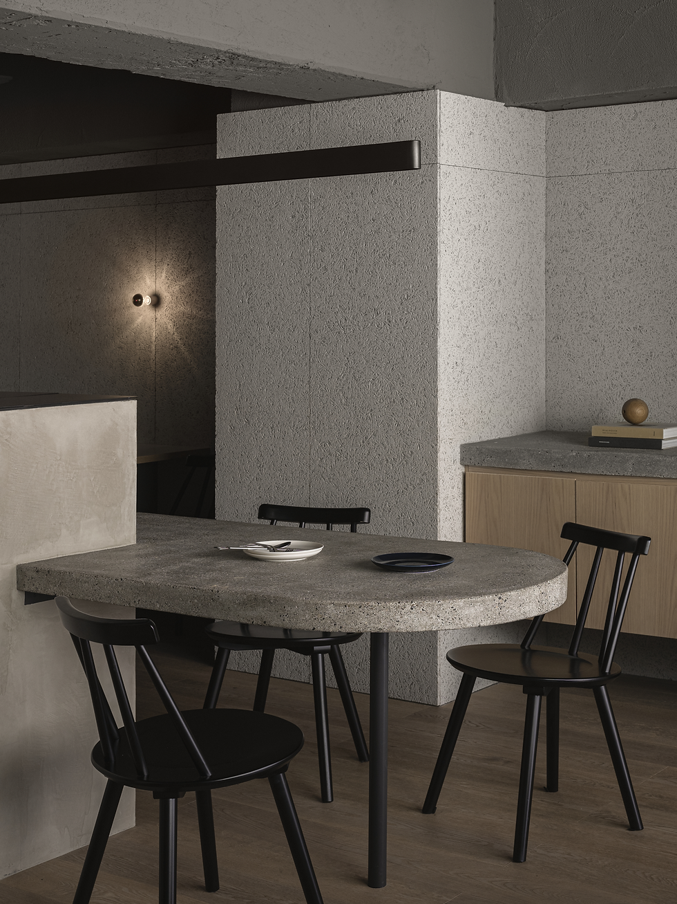 A gray-walled restaurant with a concrete table and black chairs.