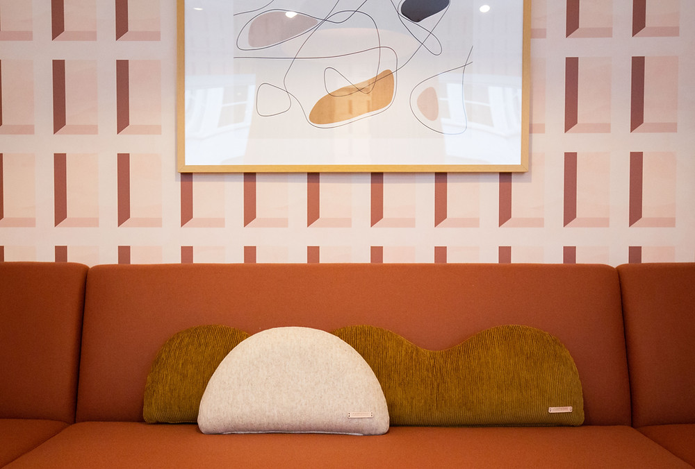 A set of curvy pillows sits on an orange couch.