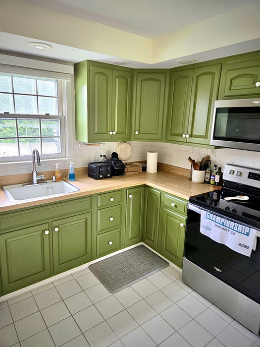 Sage green refinished kitchen cabinets with modern hardware and updated white tile backsplash in a bright corner kitchen