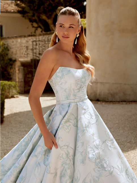 Abito da sposa principesco in broccato con corpetto senza spalline e scollatura cat-eye, cintura in vita e strascico lungo con bottoni gioiello sul retro.