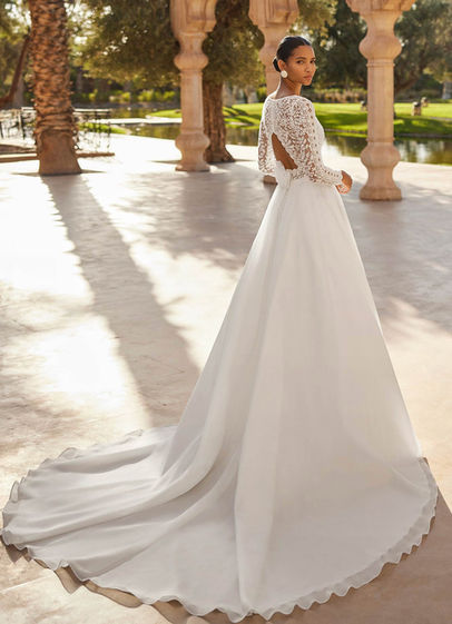 Rosa Clarà #ONASIS – abito da sposa lungo A-line in Mikado Verona con corpetto in pizzo e strass, scollo rotondo, maniche lunghe, schiena scoperta e spacco laterale.
