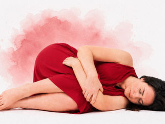 Donna in abito rosso sdraiata con le gambe raccolte mentre tiene il basso ventre per il dolore mestruale.