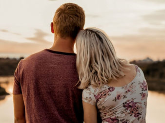 Una coppia siede abbracciata guardando il tramonto su un fiume tranquillo.