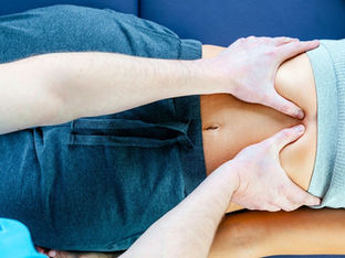 Nahaufnahme einer Person, die auf einer Liege liegt und im Bauchbereich von einer anderen Person mit beiden Händen sanft massiert oder behandelt wird.