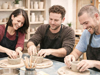 Three adults laughing while shaping clay together at a pottery wheel, expressing creative leisure in a playful and relaxed atmosphere.