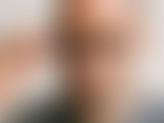 Ein glatzköpfiger Mann hebt mit einer Hand seine schwarzgerahmte Brille an, die Augenbraue leicht erhoben, mit skeptischem, wertendem Blick vor neutralem Hintergrund.