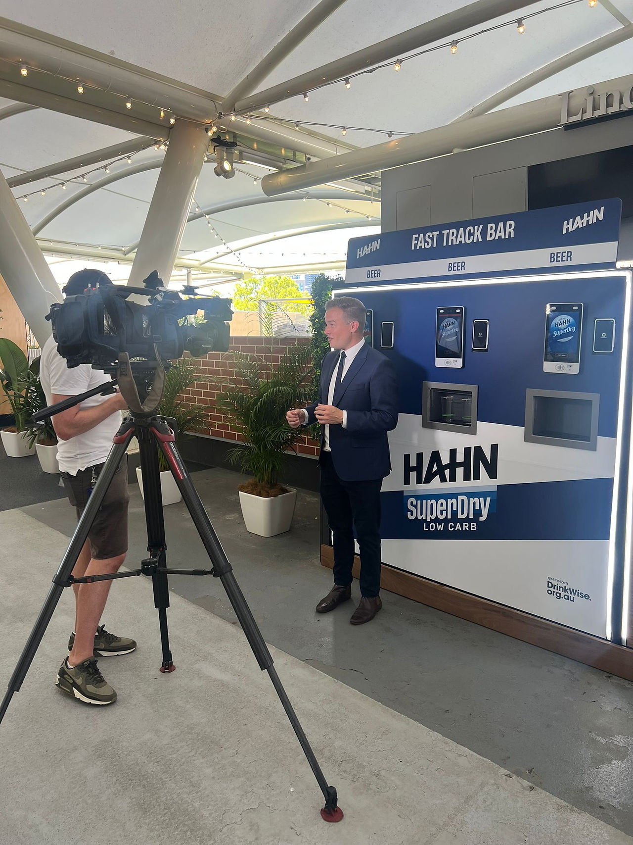 TV news reporter filmed in front of Blue and white self service beer machine