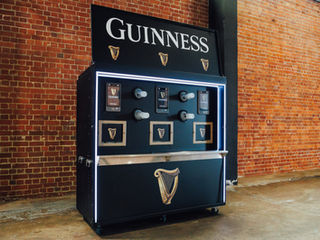 Guinness branded self-service draught beer machine against a red brick wall