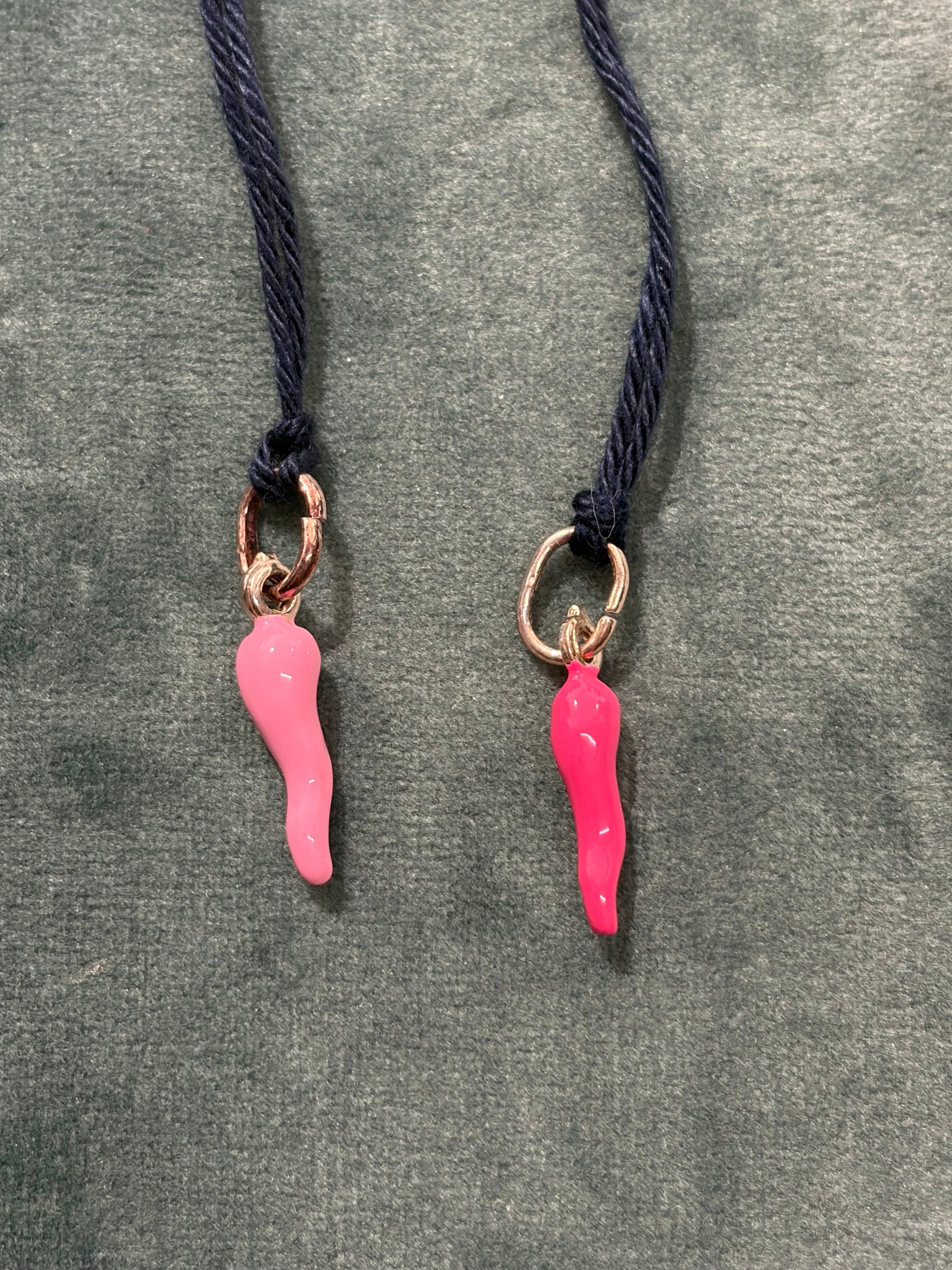 Due ciondoli a corno Le Fer rosa e fucsia con anellino metallico, fotografati su cordoncini neri