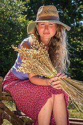 Woman in straw hat and red skirt holds dried wheat bundle.