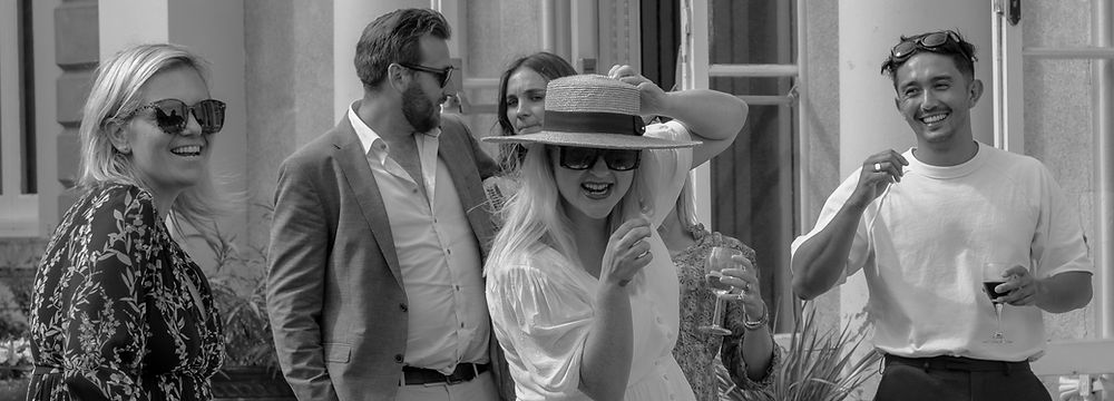 Happy friends laughing, one wears a straw hat at an outdoor event.