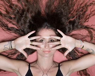 Woman with long dark curly hair, hands covering face, eyes peeking.