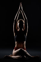 Silhouetted woman in yoga pose, hands clasped above head, dark background.