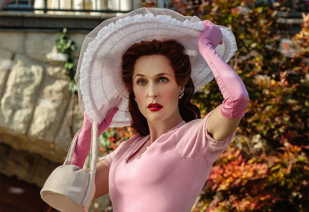 Gillian Anderson as Media in American Gods, dressed in a vintage pink ensemble with gloves and a sunhat.