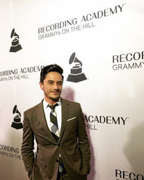 vocal coach nyc joseph stanek poses in front of a wall that says recording academy grammys on the hill