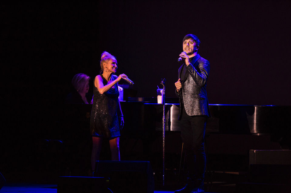 Kristin Chenoweth and Joseph Stanek perform a heartfelt duet of “The Prayer” on stage, with a grand piano and moody stage lighting setting the atmosphere.