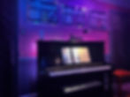 Black Kawai upright piano at Tour de Fierce Music Studio in Astoria, NYC, framed by Billboard chart plaques and illuminated with stage lighting for professional voice lessons and recording sessions.