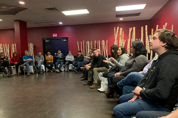 A group of adults sitting in a curved shape in an indoor space. Some of them discussing with each other