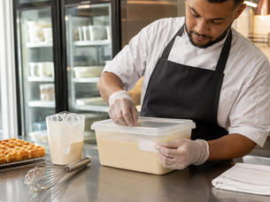 Chef labelling covered commercial waffle batter for refrigerated storage in a professional kitchen