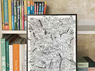 A James Illustrates art print map of The Lake District National Park sits on a book shelf in front of travel books and exposed plaster wall.