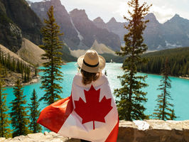 Femme portant un drapeau Canadien devant un paysage Canadien.