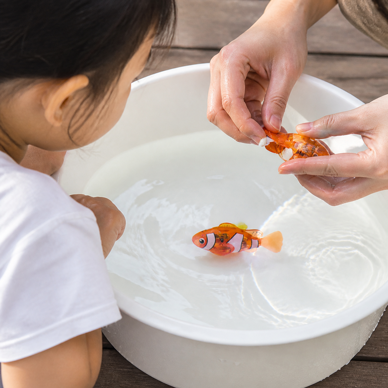 Photosensitive Swimming Clownfish Realistic Electric Pet — orange toy clownfish swimming in a clear shallow play basin while child watches from the side