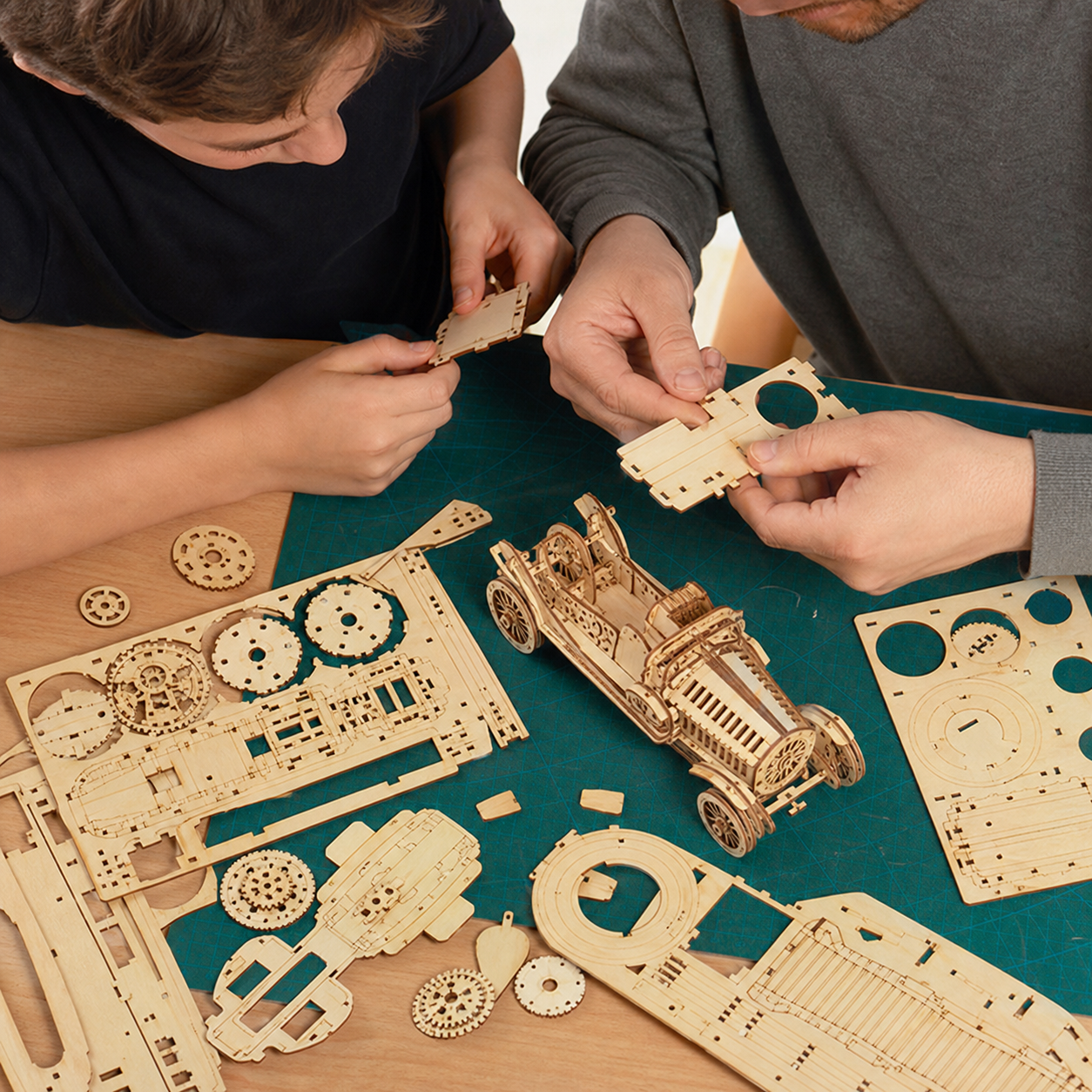 3D Car Wooden Puzzle Scale Model DIY Kit — close overhead view of hands removing and aligning laser-cut plywood parts, natural fingers
