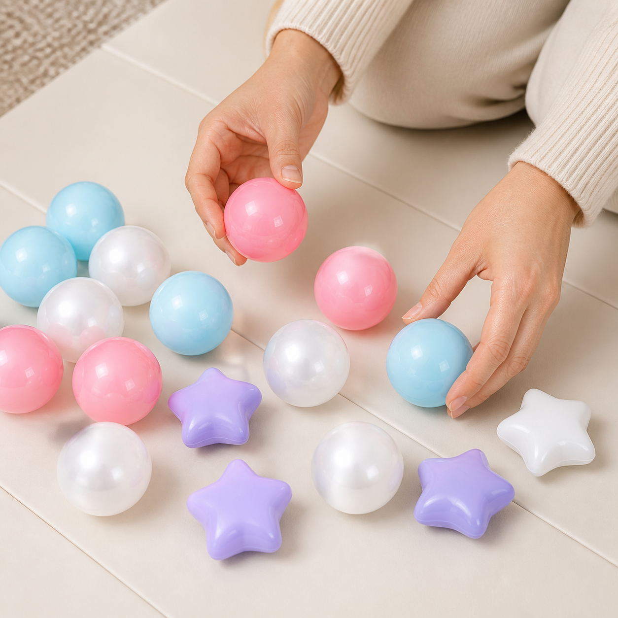 Adult hands sorting pastel round balls and star-shaped plastic pieces on a play mat
