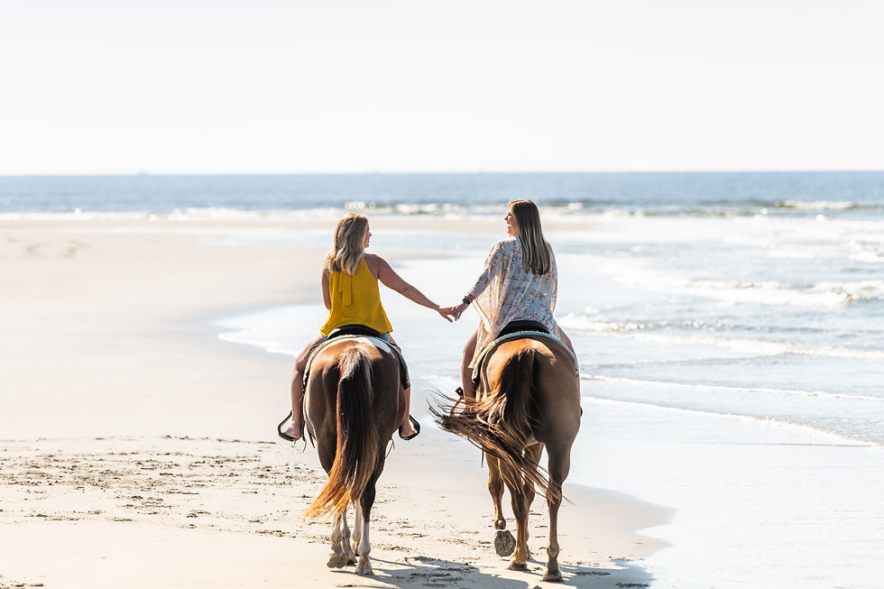 two women horseback riding on the beach while holding hands