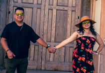 Couple holding hands, wearing sunglasses, in front of wood door.