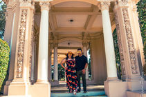 Couple posing under ornate stone pavilion with carved columns.