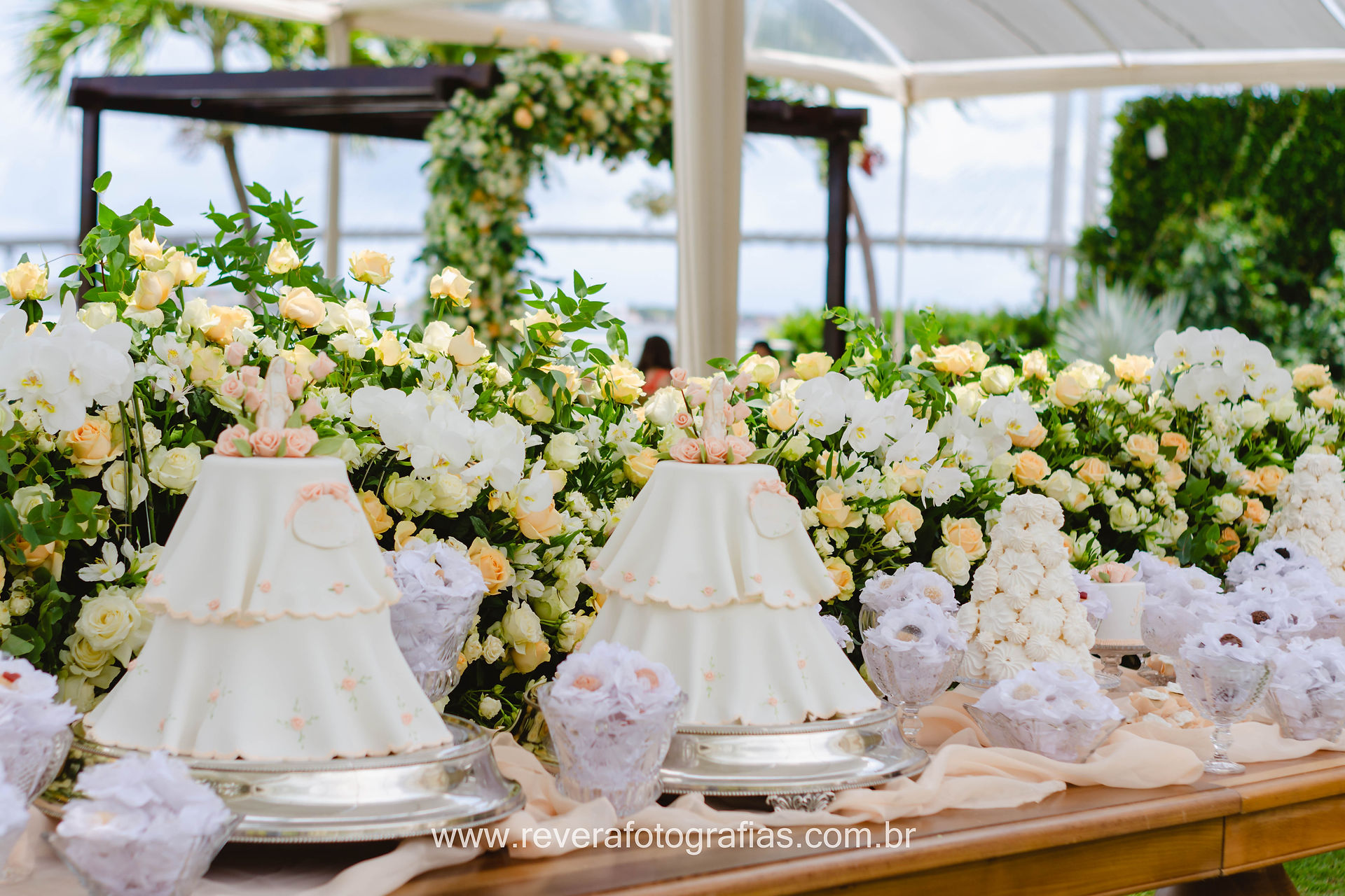 reverá fotografias: fotografia de decoração de mesa de dois bolos de dois 2 andares pasta americana delicado para batizado branco com rosê com santa em cima e flores