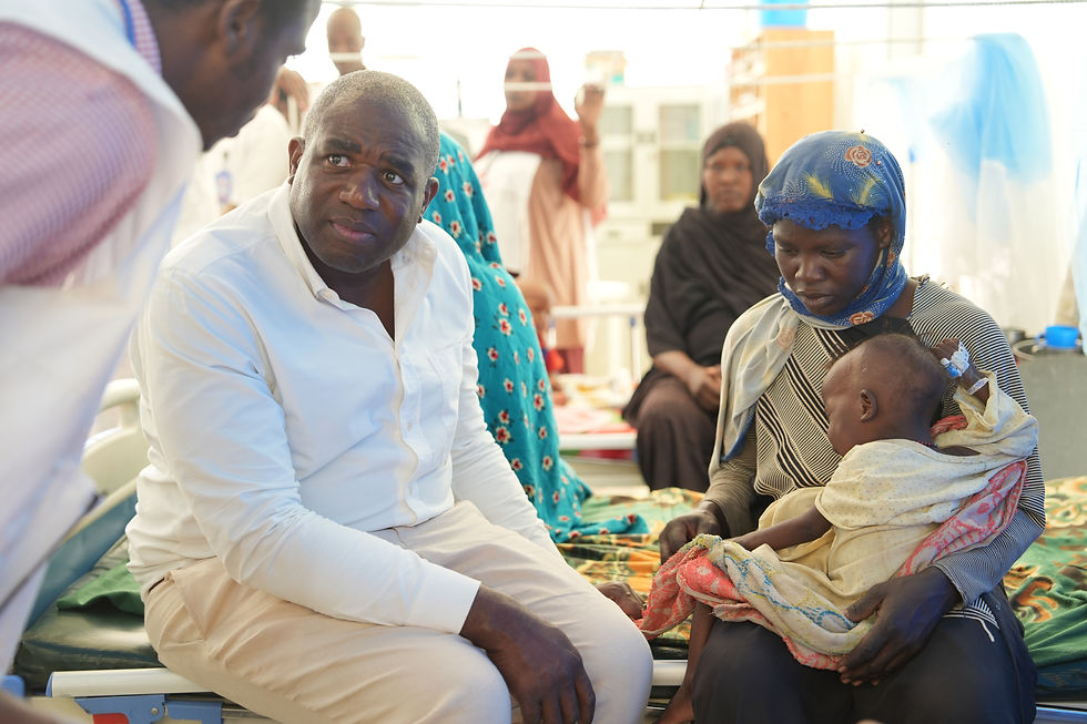 Photo d’archives de David Lammy assis auprès d’une femme tenant un enfant dans un établissement de soins à Adré, au Tchad.