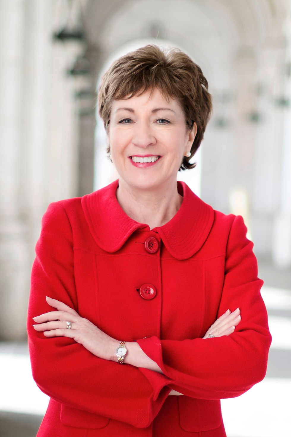 Susan Collins pose en veste rouge dans un corridor à colonnes.